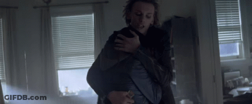 A Man Is Holding Another Man In His Arms In A Room With Blinds GIF