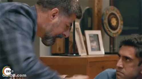 A Man Is Holding Another Man 'S Hand While Sitting At A Table In A Living Room . GIF