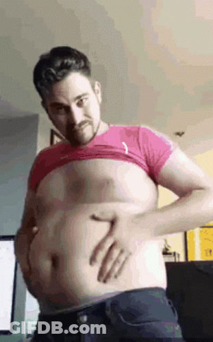 A Man Is Holding His Belly With His Hands While Wearing A Pink Shirt . GIF