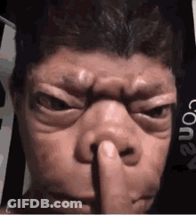 A Man Is Holding His Finger To His Nose . GIF