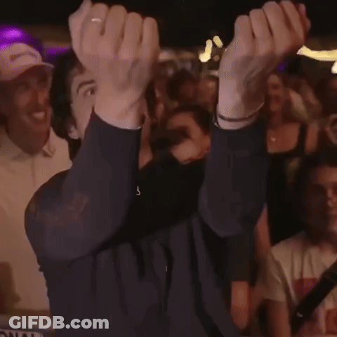 A Man Is Holding His Hands Up In The Air While A Crowd Watches GIF