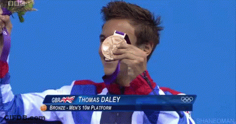 A Man Is Holding Up A Gold Medal With The Name Thomas Daley On The Bottom GIF