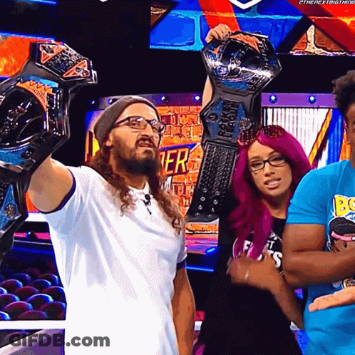 A Man Is Holding Up A Wrestling Championship While Standing Next To A Woman With Pink Hair GIF