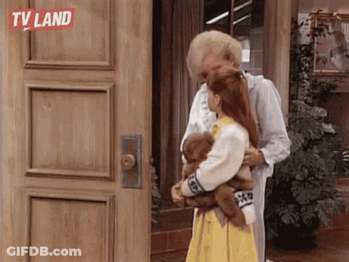 A Man Is Hugging A Little Girl Who Is Holding A Teddy Bear In Front Of A Wooden Door . GIF