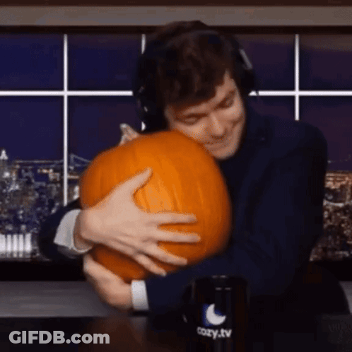A Man Is Hugging A Pumpkin In Front Of A Cozy Tv Mug . GIF