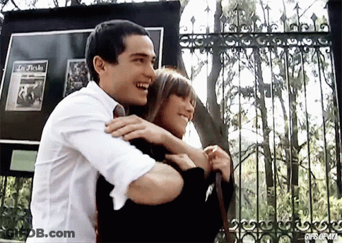 A Man Is Hugging A Woman In Front Of A Sign That Says " In Flecha " GIF