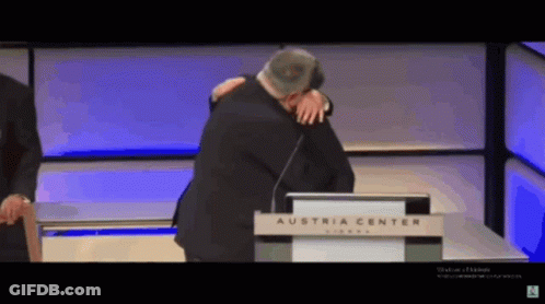 A Man Is Hugging Another Man In Front Of A Podium That Says Austria Center GIF