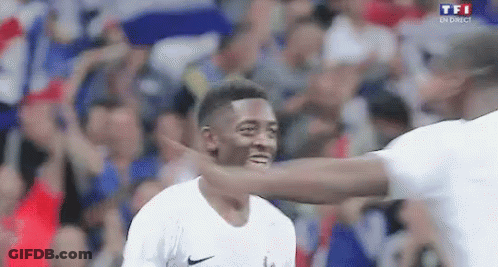 A Man Is Hugging Another Man On A Soccer Field While A Crowd Watches . GIF