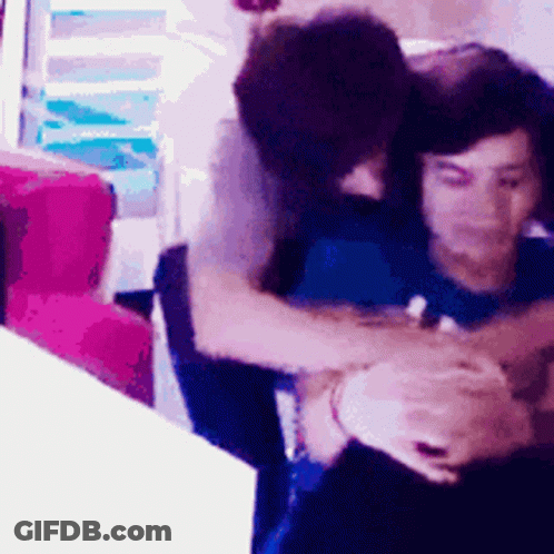 A Man Is Hugging Another Man While Sitting In A Chair GIF