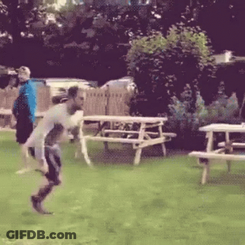 A Man Is Jumping In The Air In A Field With Picnic Tables In The Background GIF