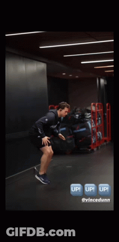 A Man Is Jumping In The Air In A Gym With A Sign That Says Up GIF