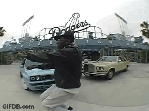 A Man Is Jumping In The Air In Front Of Dodgers Stadium GIF