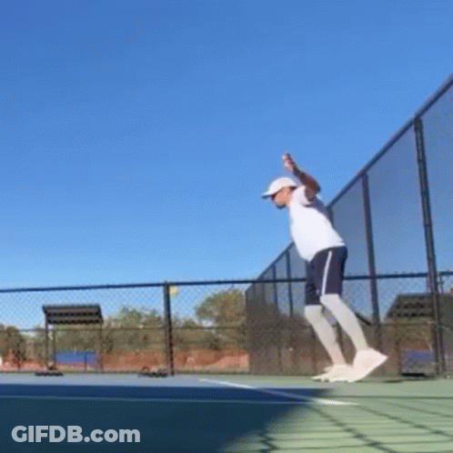 A Man Is Jumping In The Air While Holding A Tennis Racquet On A Tennis Court . GIF