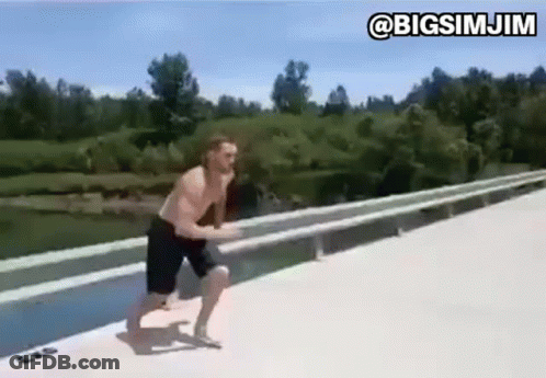 A Man Is Jumping Into A Body Of Water From A Bridge . GIF