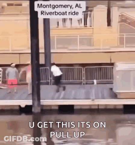 A Man Is Jumping Into A Body Of Water Next To A Sign That Says Montgomery Al Riverboat Ride GIF