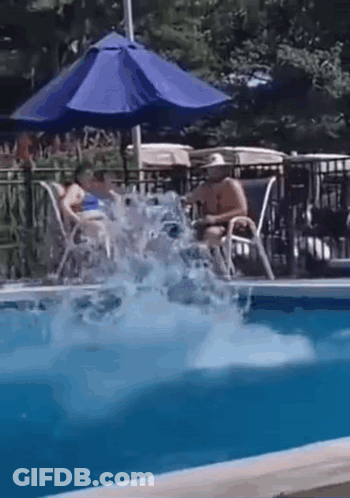 A Man Is Jumping Into A Swimming Pool While A Woman Sits On A Chair Under An Umbrella . GIF
