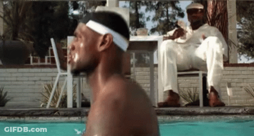 A Man Is Jumping Into A Swimming Pool While Another Man Sits On A Chair . GIF