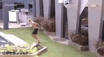 A Man Is Jumping Into A Swimming Pool While Wearing Shorts . GIF
