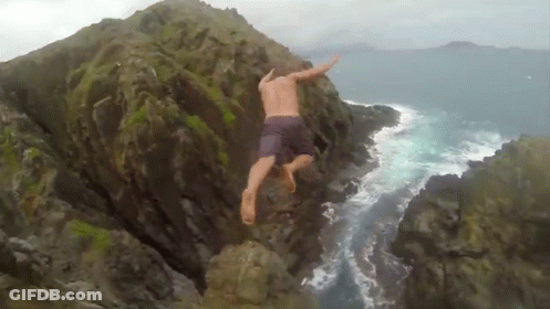 A Man Is Jumping Off A Rocky Cliff Into The Ocean GIF