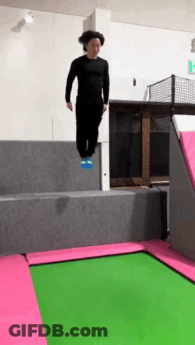 A Man Is Jumping On A Trampoline With A Pink And Green Mat . GIF
