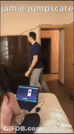 A Man Is Jumping Over A Woman Sitting On A Bed With A Laptop In Front Of Him . GIF