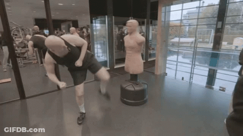 A Man Is Kicking A Punching Bag In A Gym While Another Man Watches GIF