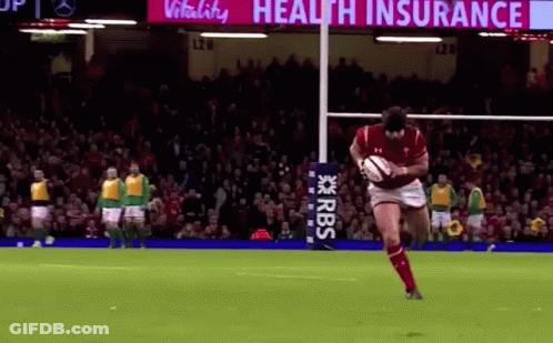 A Man Is Kicking A Rugby Ball On A Field With A Sign That Says Health Insurance In The Background . GIF