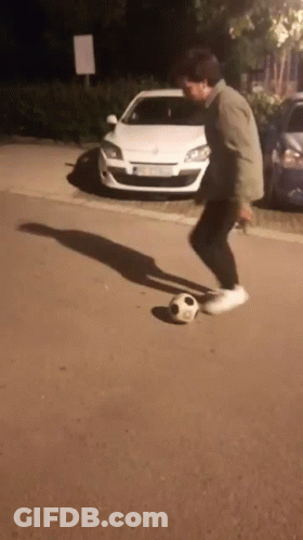 A Man Is Kicking A Soccer Ball On The Sidewalk In Front Of A White Car GIF