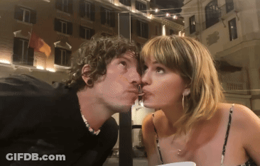 A Man Is Kissing A Woman On The Cheek In Front Of A Building GIF