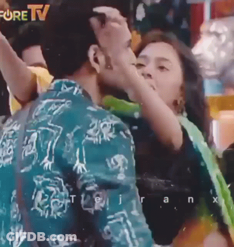 A Man Is Kissing A Woman On The Cheek In Front Of A Fore Tv Sign GIF