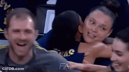 A Man Is Kissing A Woman On The Cheek While Sitting In A Basketball Stadium . GIF
