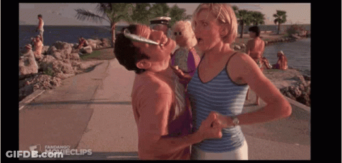 A Man Is Kissing A Woman On The Cheek While Standing On A Beach . GIF