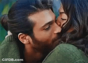 A Man Is Kissing A Woman On The Cheek While They Are Hugging . GIF