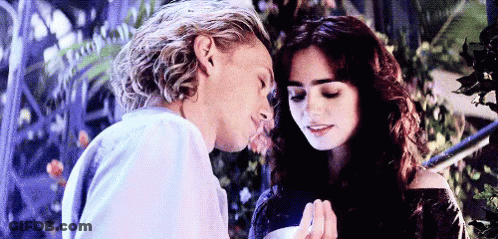 A Man Is Kissing A Woman On The Forehead While Holding Her Hand . GIF