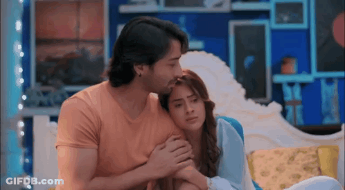 A Man Is Kissing A Woman On The Forehead While They Are Sitting On A Couch In A Living Room . GIF