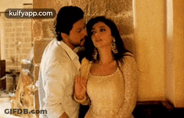 A Man Is Kissing A Woman On The Neck In Front Of A Wall . GIF