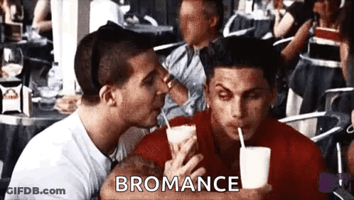 A Man Is Kissing Another Man On The Cheek While Holding A Drink . GIF