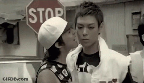 A Man Is Kissing Another Man On The Cheek While Standing In Front Of A Stop Sign . GIF