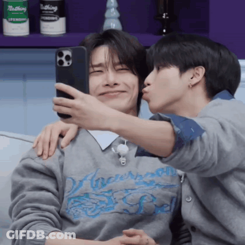 A Man Is Kissing Another Man On The Cheek While They Take A Selfie GIF