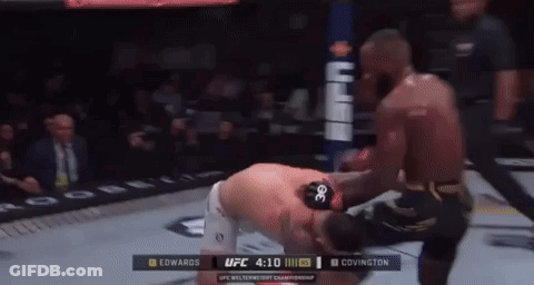 A Man Is Kneeling Down In A Boxing Ring While Another Man Kicks Him . GIF