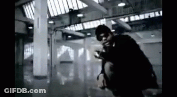 A Man Is Kneeling Down In A Dark Room With A Gun . GIF