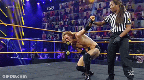 A Man Is Kneeling Down In A Wrestling Ring With A Referee Standing Behind Him . GIF