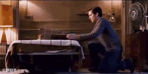 A Man Is Kneeling Down In Front Of A Bed In A Bedroom . GIF