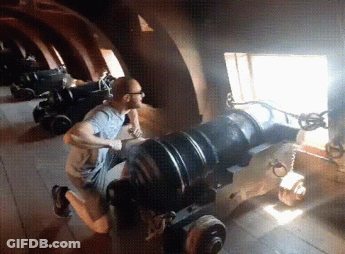 A Man Is Kneeling Down In Front Of A Cannon With A Window In The Background GIF