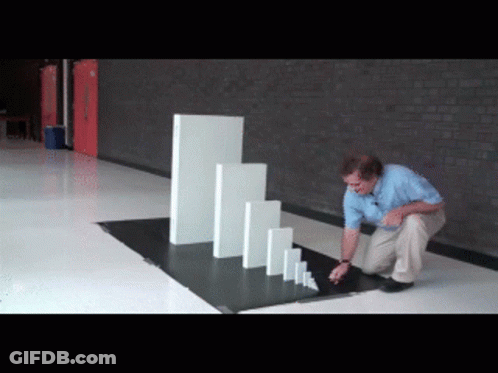 A Man Is Kneeling Down In Front Of A Row Of Dominoes GIF