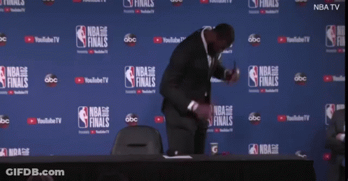 A Man Is Kneeling Down In Front Of A Wall That Says Nba Finals On It GIF