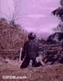 A Man Is Kneeling Down In The Dirt In A Field . GIF