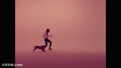 A Man Is Kneeling Down Next To A Small Dog In A Pink Background . GIF