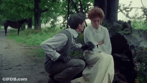 A Man Is Kneeling Down Next To A Woman Sitting On A Bench With A Horse In The Background . GIF