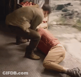 A Man Is Kneeling Down Next To Another Man In Front Of A Crate Of Apples GIF